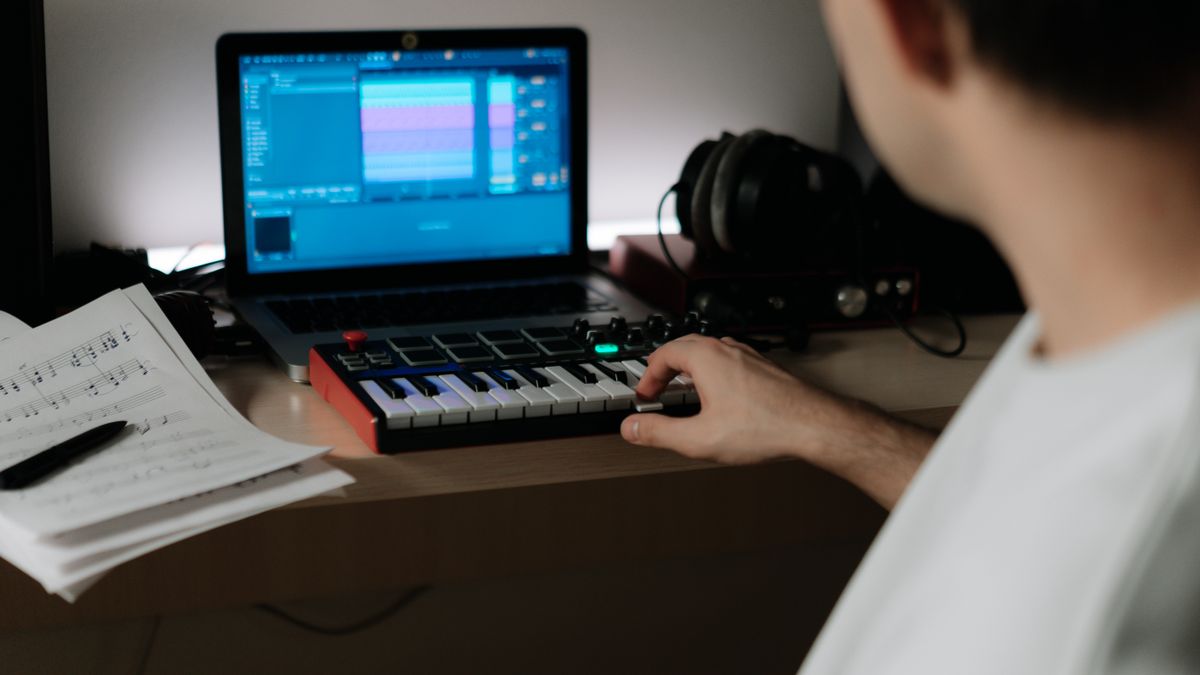 Creator using a synthesizer and laptop for digital music production